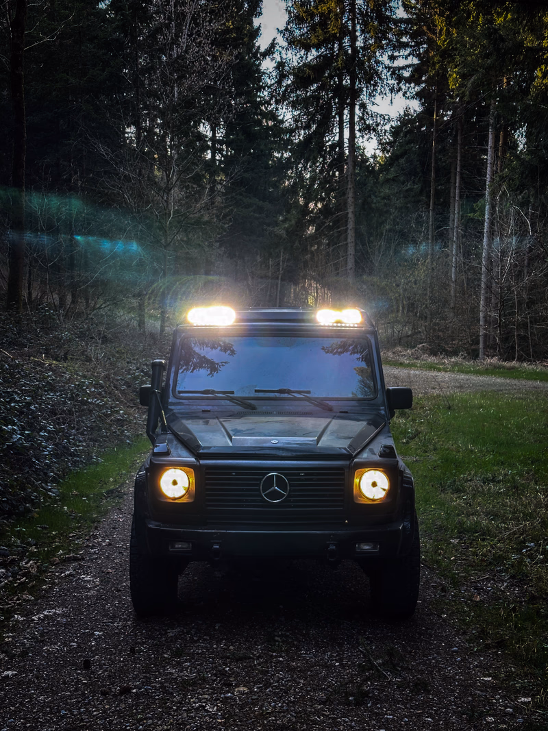 Dunkle G-Klasse mit Walger Works Dachtraeger im Wald, Scheinwerfer an